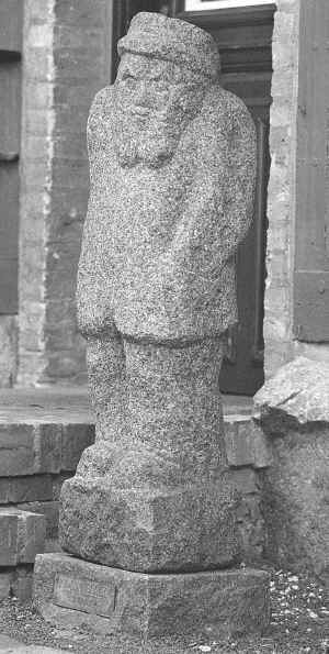 Granitskulptur af en varmt påklædt mandsling med hat og fuldskæg.